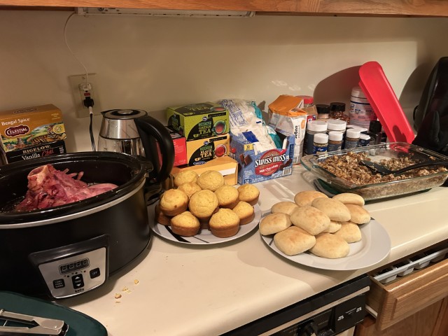 Ham, dinner rolls, cornbread, and stuffing sitting on a counter.